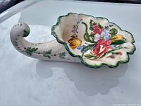 Angled side view of the ceramic centerpiece showing the hand painted floral design on the scalloped bowl and curved handle.