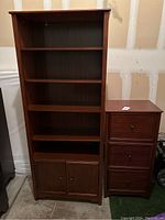 Photo showing the wooden bookcase with four open shelves and a bottom two-door cabinet, next to a wooden file cabinet with three drawers.
