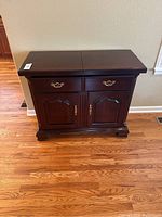Front view of dark brown wooden serving buffet showing two drawers with brass handles and two paneled cabinet doors with brass knobs.