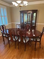 Full view of cherry wood dining table with eight chairs and buffet cabinet in the background, showing overall set condition and style.
