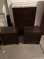 Photo of dark brown tall dresser with four drawers and two nightstands in front.