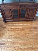 Front view of wooden entertainment cabinet showing four doors including two glass-paneled center doors, two wooden drawers on top, and wood finish with knobs.