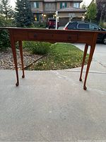 Front view of wooden entry table showing overall shape, drawer with handles, and tapered legs.
