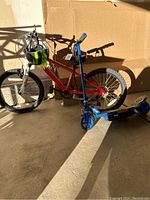 Side view of red Diamondback kids bike and blue Razor scooter leaning against a cardboard box in a concrete floor area