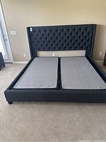 Front angled view of dark grey upholstered king size bed frame with tufted headboard and split base for two mattresses.