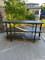 Front view of grey wood shelf unit with three shelves and black metal frame outdoors on concrete surface.