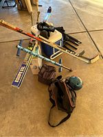 Overview of mixed sports equipment including hockey sticks, baseball bats, skis, bowling ball, boxing gloves, cooler, net, and carrying bags.