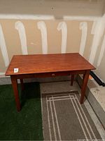 Full view of the rectangular wooden table or desk with tapered legs and single drawer.