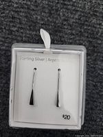 Pair of sterling silver earrings in clear plastic packaging with card labeled 'Sterling Silver' and price of $20.