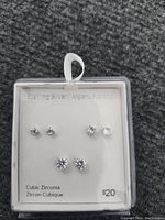 Photo of a set of six pairs of sterling silver cubic zirconia stud earrings, displayed in original packaging. Each pair varies in cubic zirconia stone size, labeled $20.