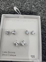Photo showing six pairs of sterling silver stud earrings with cubic zirconia stones in heart, round, and square shapes displayed on a white card.