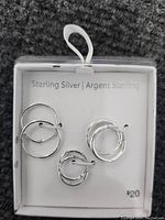 Clear plastic box containing three pairs of sterling silver hoop earrings in different sizes, labeled 'Sterling Silver | Argent Sterling'.