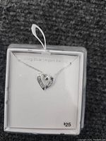 Photo of a sterling silver necklace with a heart-shaped pendant displayed in packaging on a grey carpet background.