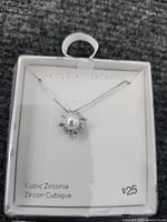 Necklace displayed in white box with brand and price information, showing sterling silver chain and pendant with pearl and cubic zirconia stones.