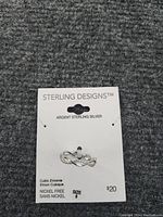 Photo shows a sterling silver ring size 8 attached to the original Sterling Designs packaging card. The ring features an infinity design with embedded cubic zirconia stones.