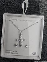 Photo of sterling silver necklace with cubic zirconia cross pendant and pair of matching cubic zirconia stud earrings in retail display packaging.