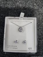 Sterling silver jewelry set displayed in a white box, consisting of a pear-shaped cubic zirconia pendant necklace and matching cubic zirconia stud earrings. The packaging indicates the materials as sterling silver and cubic zirconia with a price tag of $25.