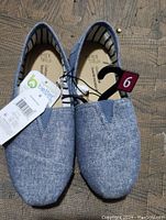 Photo shows a pair of new women's slip-on casual shoes size 6 in light blue chambray fabric with original tags and size label attached, front view.