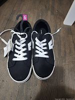 Front view of the black sneakers showing white laces and side details, new with size tag attached.