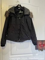 Front view of a black Bench hooded jacket hanging on a hanger, showing fleece-lined interior collar and faux fur on the hood edges.