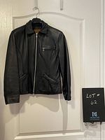 Front view of black leather bomber jacket by Esprit Sport hanging on a door, showing zipper and pockets.