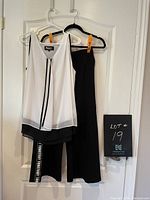 Front view of black and white sleeveless blouse with black cozy pants hanging on door