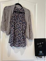 Photo of the blue floral camisole top paired with the grey crocheted shrug hanging on a black hanger against a white door