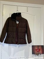 Front view of dark brown quilted bomber jacket hanging on white door, showing faux fur collar and front zipper.