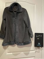 Front view of the grey cape style coat with faux fur trim on collar, cuffs, and hem, hanging on a white door.