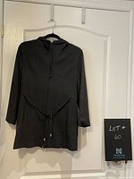 Full front view of charcoal grey coat with hood, zipper, pockets, and string belt on hanger against door.