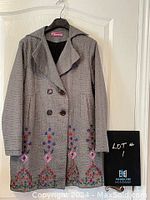 Front view of the grey cloth coat showing double-breasted buttons and embroidered floral design on the lower front hem.