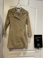 Camel coloured corduroy jacket hanging on a white hanger on a door, showing front fully buttoned double-breasted style with lapels, pockets, and button details on cuffs.