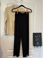 Photo of black pull-on dress pants hanging on black hanger alongside gold blouse on white hanger, both displayed on a white door.