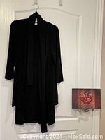 Black long jacket with three-quarter sleeves and matching scarf hanging on a hanger against a white door.
