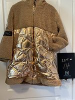 Front view of the gold women's winter jacket hanging on a door. Shows tan fleece top and metallic gold quilted bottom with front zipper.