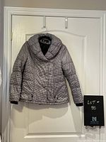 Front view of black and white houndstooth pattern short jacket with large collar and double-breasted button front, hanging on door.