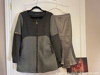 Grey two-tone jacket hanging on a door, showing front view with zip and quilted pattern on lower body and upper sleeves.