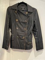 Front view of black leather jacket showing double-breasted button closure, asymmetrical zipper, belt buckle, and seam detailing.