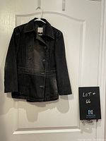 Full view of the front of the long dark denim jacket hanging on hanger against white door