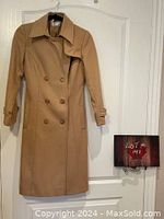 Full frontal view of the camel colored Pro Mod maxi coat hung on a door, showing the double breasted button detail, collar, and belt.