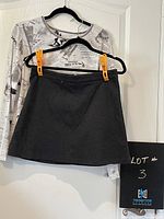 Black and white newspaper print long sleeve crew neck top hanging with charcoal grey mini skirt clipped to a black hanger against white door background.