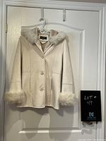 Novelti cream winter jacket with faux fur trim on hood and cuffs hanging on a white door, showing front and buttons.