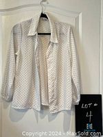 White long sleeve button-up shirt with small black polka dots on a hanger viewed from front, showing collar, button closure, and sleeves