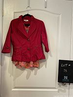 Red short jacket with 3/4 sleeves paired with colorful sleeveless floral blouse underneath, hanging on a hanger against a door.