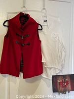 Reversible red and red tartan vest alongside white button-up top hanging on hangers
