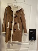 Front view of brown sheepskin look coat hanging on door, showing toggle buttons and faux shearling trim