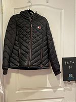 Front view of Tommy Hilfiger black quilted bomber jacket with hood and zippered front, showing jacket fully visible on hanger.