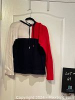 Front view of Tommy Hilfiger pullover sweater with hood hanging on hanger, showing tri-color design (white, red, navy blue).
