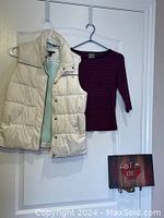 White quilted puffy vest and burgundy striped top hanging on hooks on door.