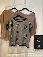 Three oversized pullover tops hung on hangers against a white door, showing variety in designs and shapes.